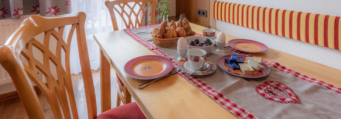 An inviting table with breakfast items in a cozy room. The table is set with dishes and a floral decoration. - Haus Edmund - Sölden