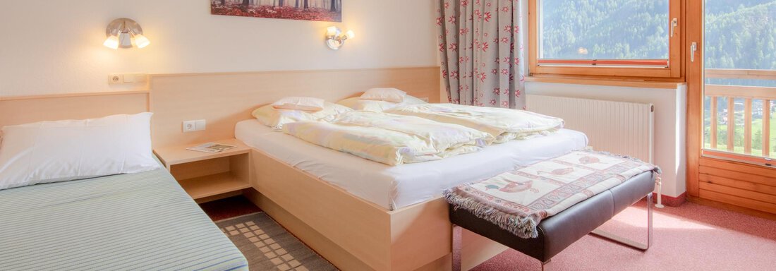 A cozy hotel room with two beds and a table. Large windows offer a view of nature. - Haus Edmund - Sölden