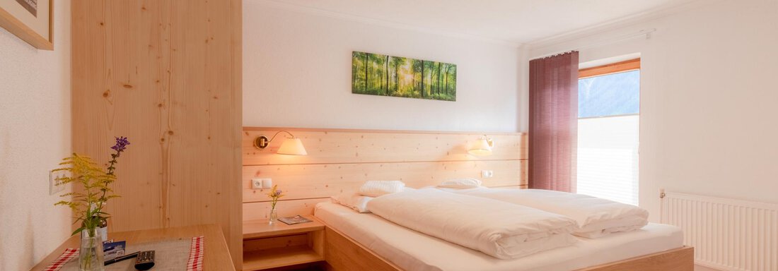 Arnika Schlafzimmer Haus Edmund A cozy bedroom with wood paneling and a large bed. The walls are painted in light colors, and a window provides plenty of natural light. - Haus Edmund - Sölden