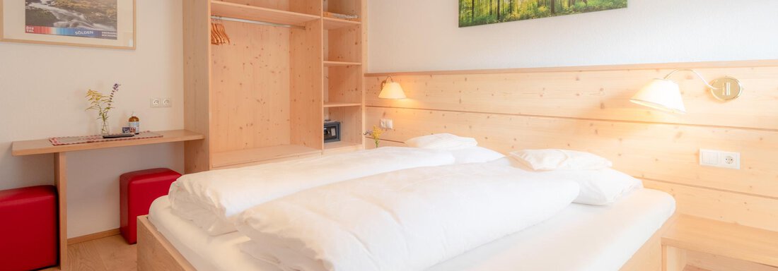 A modern bedroom with a large bed and light wooden interior. There is a desk and colorful chairs, as well as a picture with a forest motif on the wall. - Haus Edmund - Sölden
