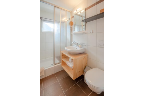 A modern bathroom with a shower and sink. Wooden shelves provide space for towels and toiletries. - Haus Edmund - Sölden