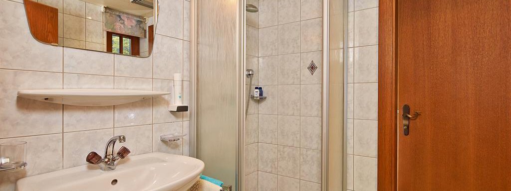 A modern bathroom with a shower cubicle and a sink. The walls are covered with white tiles, and there is a wooden frame for the door. - Haus Fontana - Sölden