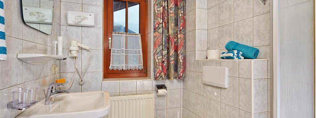 A clean bathroom with bright tiles and a window. It includes a sink, a toilet, and towels. - Haus Fontana - Sölden