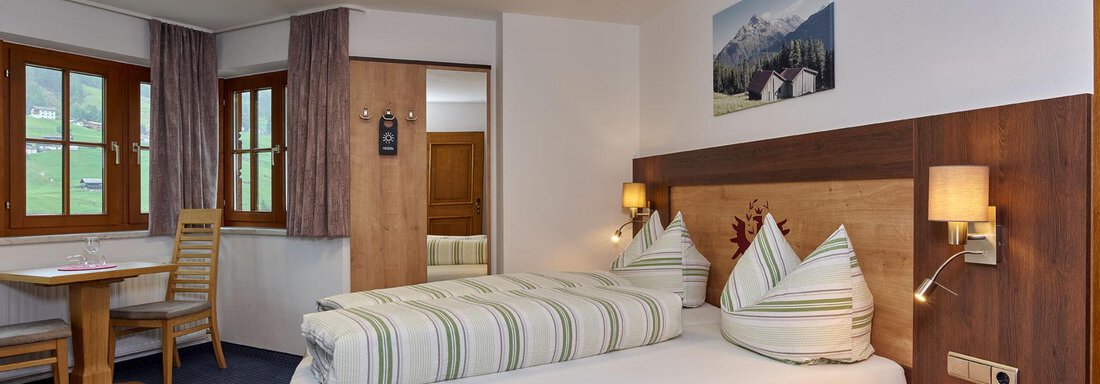Doppelzimmer A cozy hotel room with wooden decor and two beds. The room is bright and has large windows with a view of the mountains. - Haus Fontana - Sölden