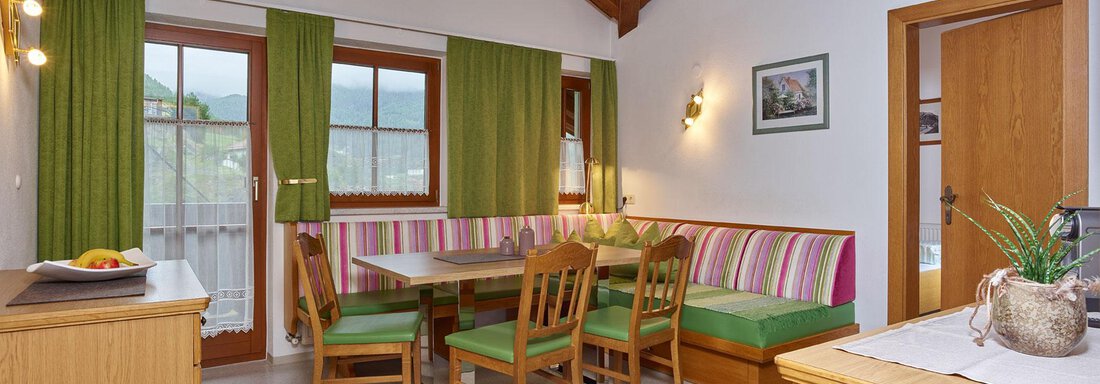 A cozy interior with wood paneling and high ceilings. There is a dining area with colorful benches and a view of the outdoor area. - Haus Fontana - Sölden