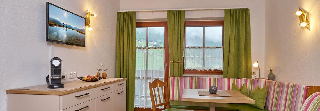 A cozy dining area with a wooden bench and colorful cushions. Large windows let in plenty of light and offer a view outside. - Haus Fontana - Sölden
