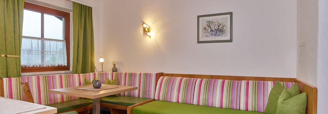 A cozy living area with colorful benches and a table. The windows let in plenty of daylight, and the walls are painted in light tones. - Haus Fontana - Sölden