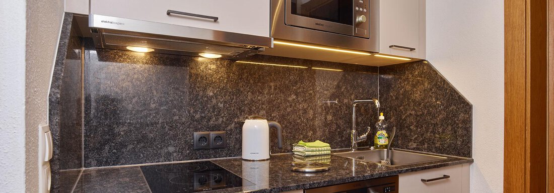 A modern kitchen with a dark granite countertop and modern appliances. There is a microwave oven, cooktops, and some kitchen utensils. - Haus Fontana - Sölden