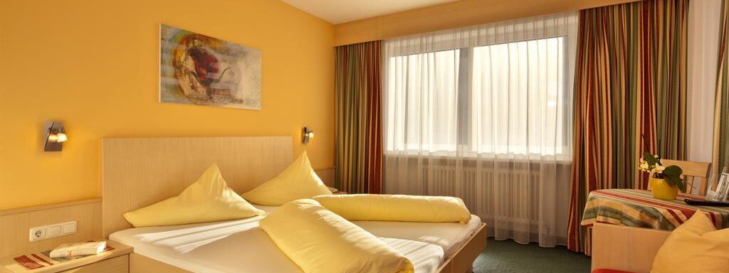 Zimmer A cozy hotel room with a double bed and yellow pillows. Large windows provide plenty of natural light and a friendly atmosphere. - Haus Fridolin - Sölden