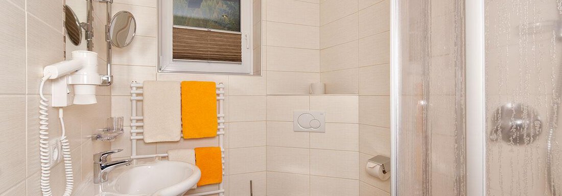 A modern bathroom with a shower, sink, and toilet. Towels in orange and beige provide a colorful accent. - Haus Fridolin - Sölden