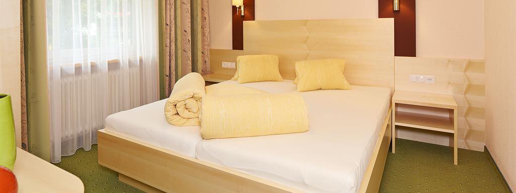 A bright bedroom with a large double bed and soft colors. The room also includes a bedside table and windows with curtains. - Haus Fridolin - Sölden