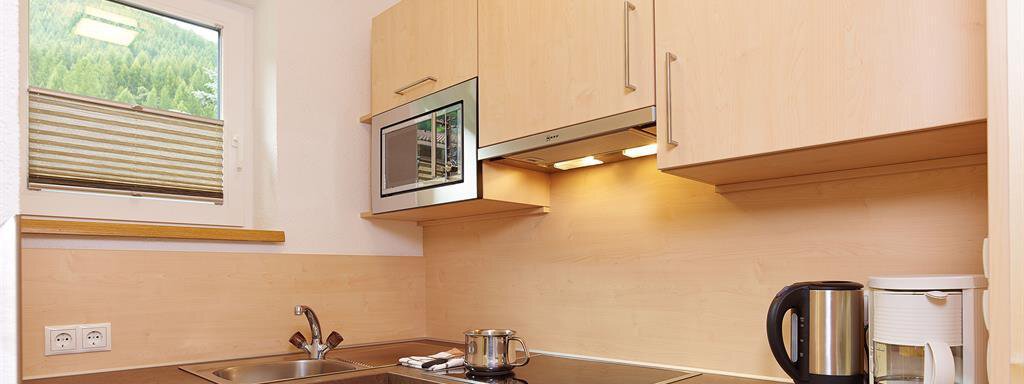 A modern kitchen with light wooden cabinets and a brown countertop. It is equipped with a stove, a microwave, and a coffee machine. - Haus Fridolin - Sölden