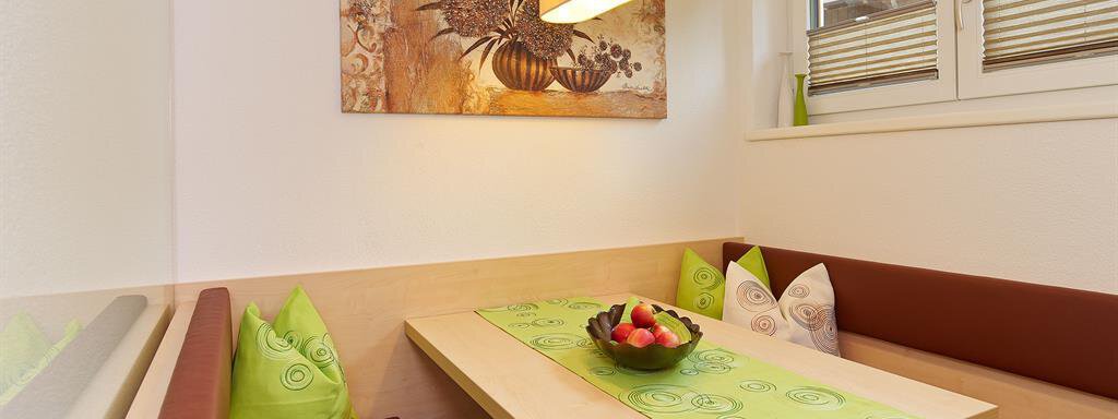 A cozy dining area with a wooden table and comfortable benches. A bowl of fresh fruit sits on the table, and the walls are adorned with artwork. - Haus Fridolin - Sölden