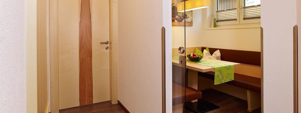 A bright hallway with wooden flooring and a modern glass door. On the left side, there is a cozy seating area with a table and lovely decor. - Haus Fridolin - Sölden
