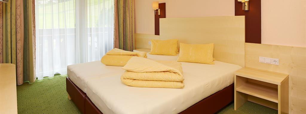A cozy bedroom with a double bed and yellow pillows. Large windows provide plenty of daylight and a view of the outside. - Haus Fridolin - Sölden