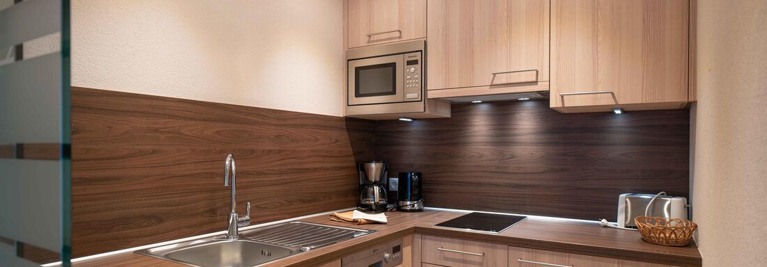 A modern kitchen with wooden fronts and smooth surfaces. The equipment includes a sink, microwave, and coffee machine. - Haus Fridolin - Sölden
