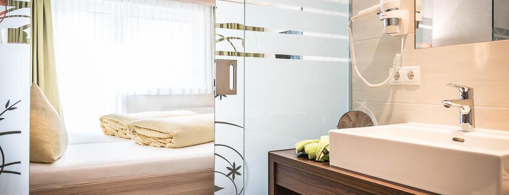 A modern bathroom with an elegant sink and plenty of natural light. In the background, a cozy bedroom can be seen with a large window. - Haus Fridolin - Sölden