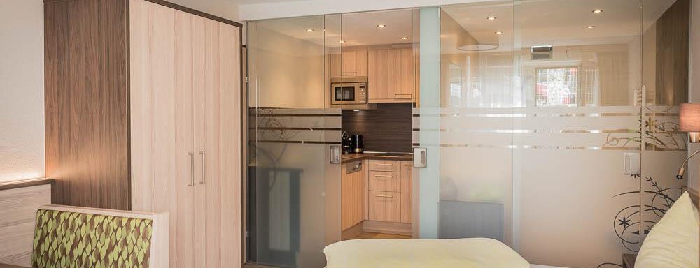 A modern room with a double bed and a cozy seating area. The kitchen is separated by glass walls and is well equipped. - Haus Fridolin - Sölden