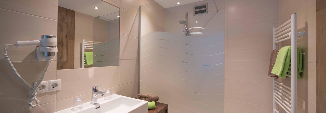 A modern bathroom with a glass shower and a sink. The walls are light, and there are fresh towels in green and brown. - Haus Fridolin - Sölden