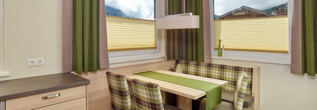 Essbereich A modern dining kitchen with a table and additional seating in neutral colors. The windows offer a view of the landscape with gentle clouds. - Haus Fridolin - Sölden