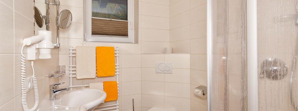 A modern bathroom with a shower, sink, and toilet. Towels in orange and yellow decorate the room. - Haus Fridolin - Sölden