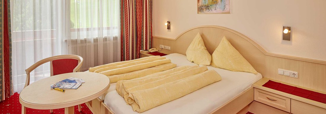 A cozy bedroom with a double bed and two large pillows. A round table stands next to the bed and large windows let in plenty of daylight. - Haus Fridolin - Sölden
