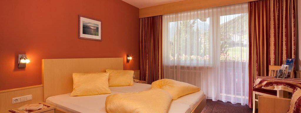 Zimmer A cozy hotel room with a double bed and orange walls. Large windows provide plenty of daylight. - Haus Fridolin - Sölden