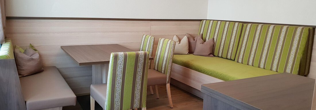 A cozy dining area with modern wooden furnishings and a seating corner in shades of green. The room offers an inviting atmosphere for shared meals. - Haus Fridolin - Sölden