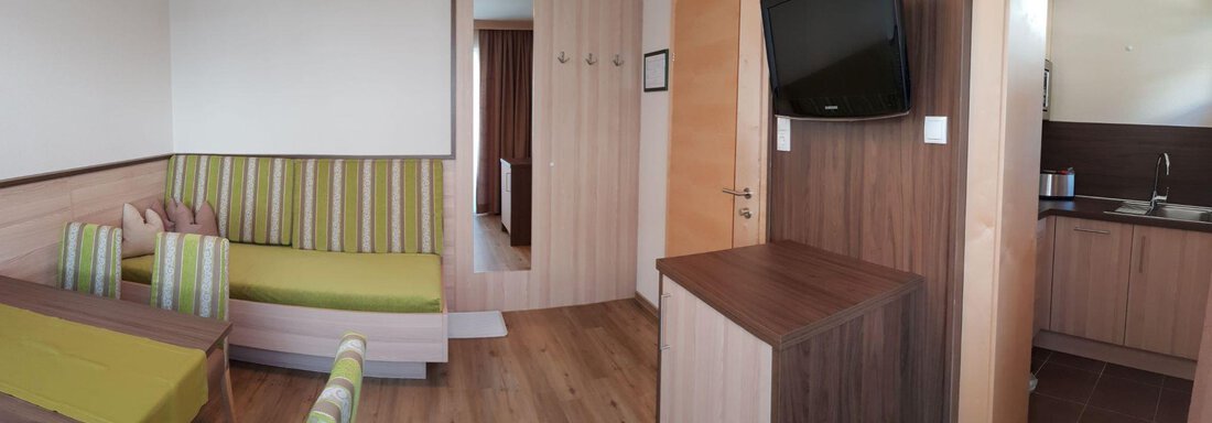 Modern living space with bright wooden flooring and a seating area. The decor is simple, featuring a television and a small kitchenette. - Haus Fridolin - Sölden