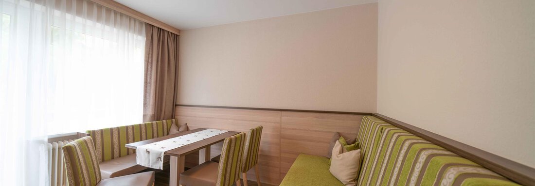 A cozy living space with a green sofa and a small dining table. Large windows let in a lot of light. - Haus Fridolin - Sölden