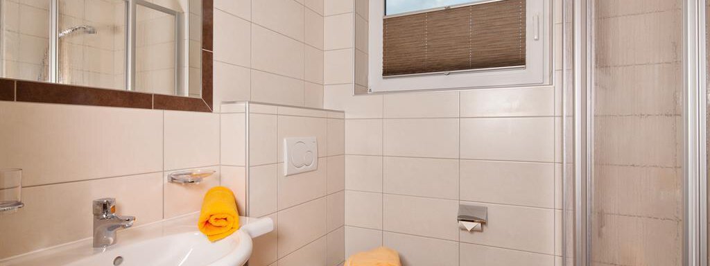 A modern bathroom with bright tiles and a shower. Orange towels are on the sink. - Haus Fridolin - Sölden