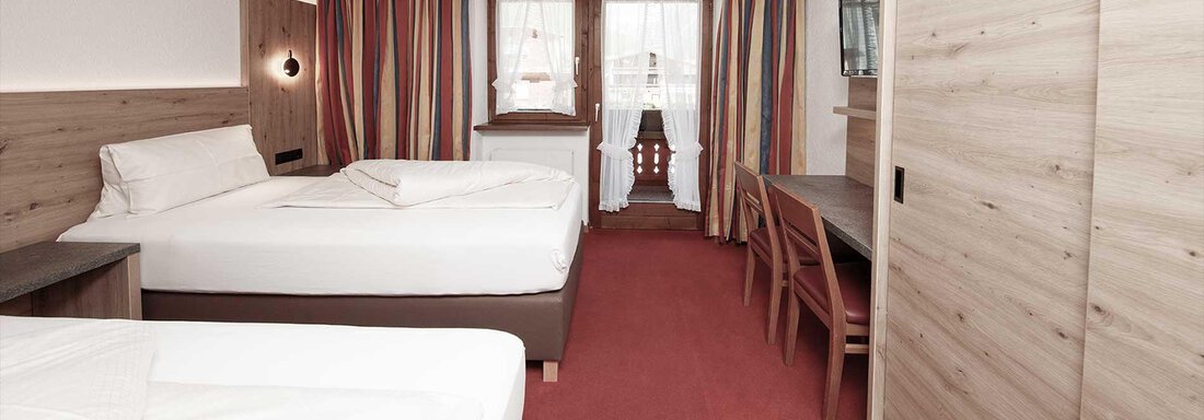 Zimmer5-A | © Falkner Georg (CC C) A cozy hotel room with two single beds and a table. Large windows let in plenty of light and offer a view of the outdoor area. - Haus Gabriela - Sölden