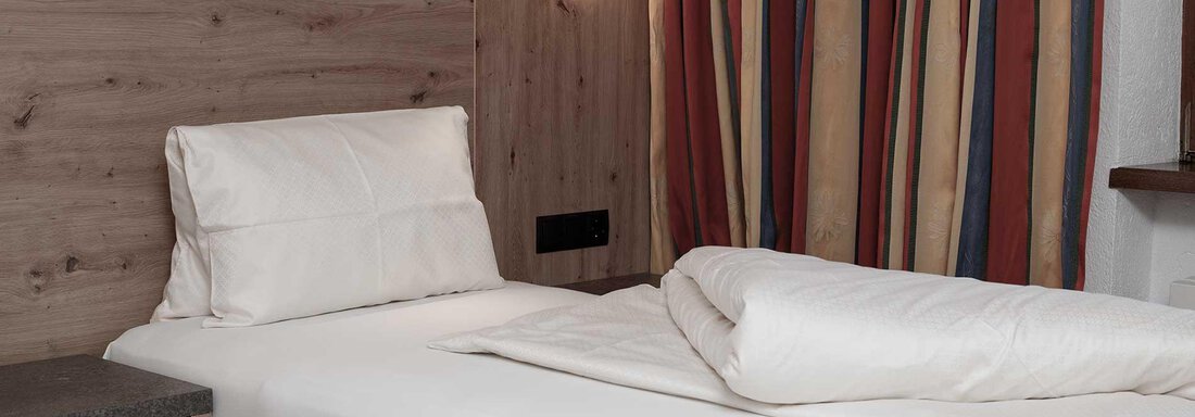 A simple bedroom with two single beds. The walls are decorated with striped curtains. - Haus Gabriela - Sölden