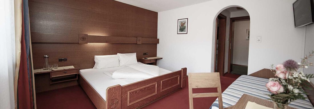 A simple, cozy bedroom with a double bed and a table. A television hangs on the wall, and there is a small table plant. - Haus Gabriela - Sölden