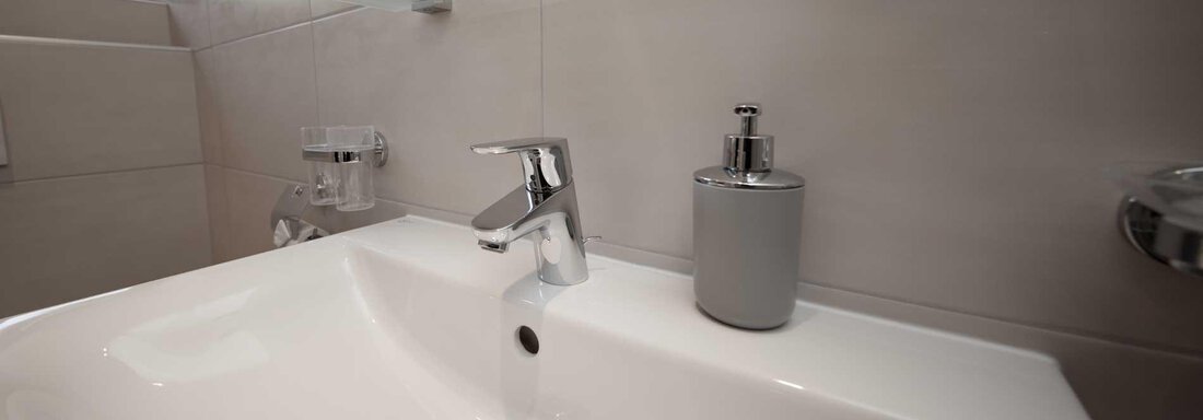 A modern bathroom with a white sink and a shiny faucet. Next to the sink is an elegant soap dispenser. - Haus Gabriela - Sölden