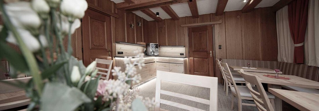 A cozy room with wooden walls and tables. In the foreground, flower arrangements can be seen, creating an inviting atmosphere. - Haus Gabriela - Sölden