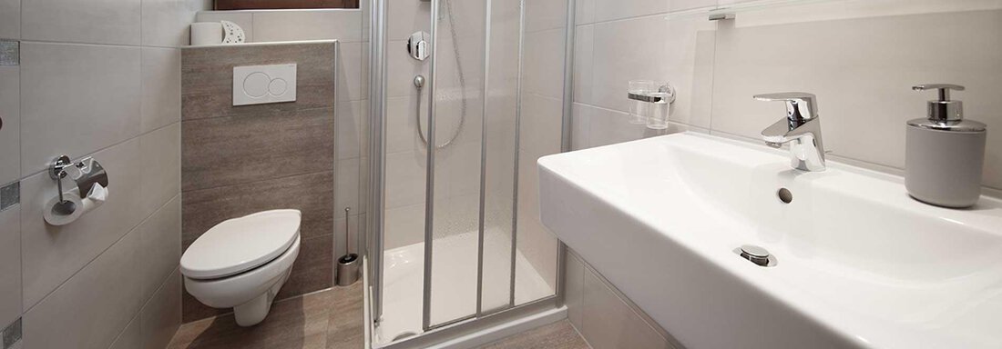A modern bathroom with a shower, a sink, and a toilet. The floor is light, and a blue bath mat is on the floor. - Haus Gabriela - Sölden
