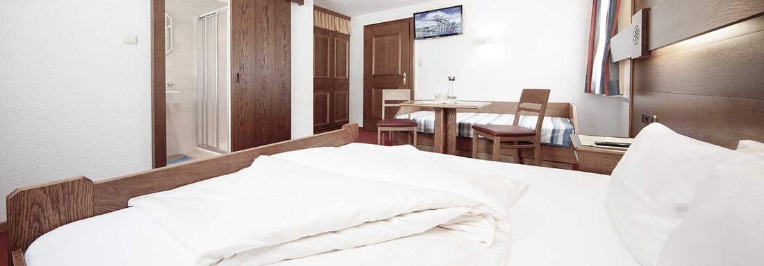 A cozy hotel room with a large bed and a dining table. The walls are in warm wood tones and a television is visible. - Haus Gabriela - Sölden