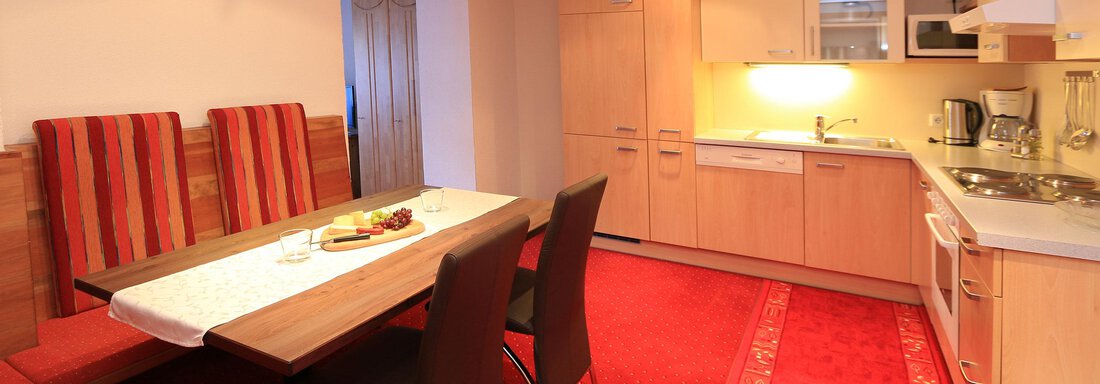 A modern kitchen with a dining area. The room is brightly and friendly furnished, with a red carpet and wooden cabinets. - Haus Gondelblick - Sölden