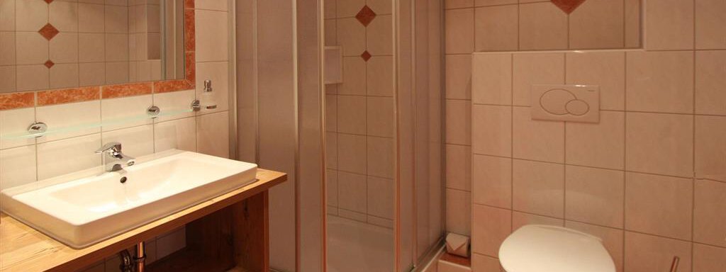 A modern bathroom with a shower, a sink, and a toilet. The walls are designed with light tiles and decorative elements. - Haus Gondelblick - Sölden