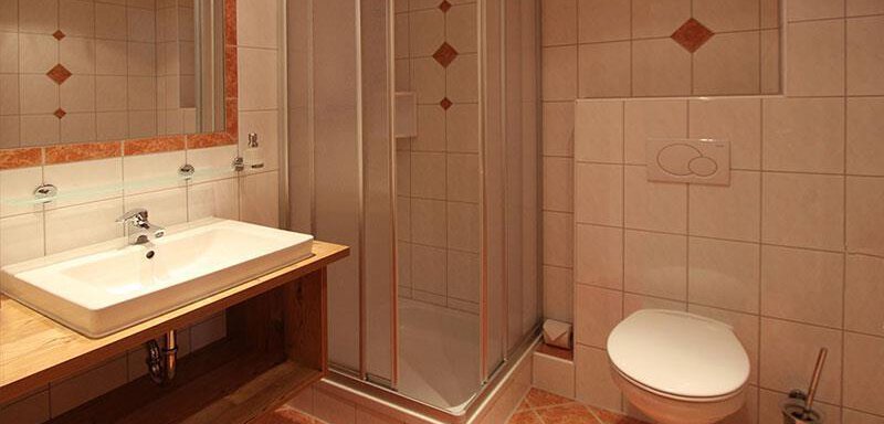 A modern bathroom with a shower, a sink, and a toilet. The walls are tiled and there is a large mirror. - Haus Gondelblick - Sölden