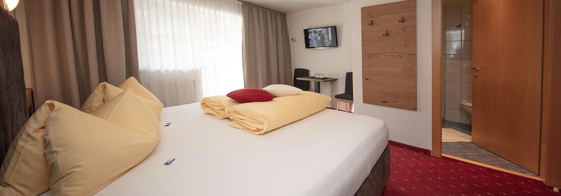 A modern hotel room with a large bed and comfortable pillows. There is a television and a view of the interior. - Haus Gondelblick - Sölden