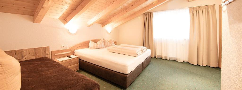A cozy bedroom with a wooden ceiling and two beds. The room has large windows that let in plenty of light. - Haus Gondelblick - Sölden