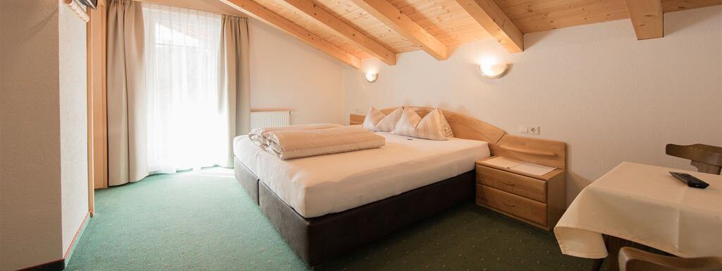 A cozy bedroom with a double bed and wooden beam ceiling. There is a small table and chairs as well as access to the balcony. - Haus Gondelblick - Sölden