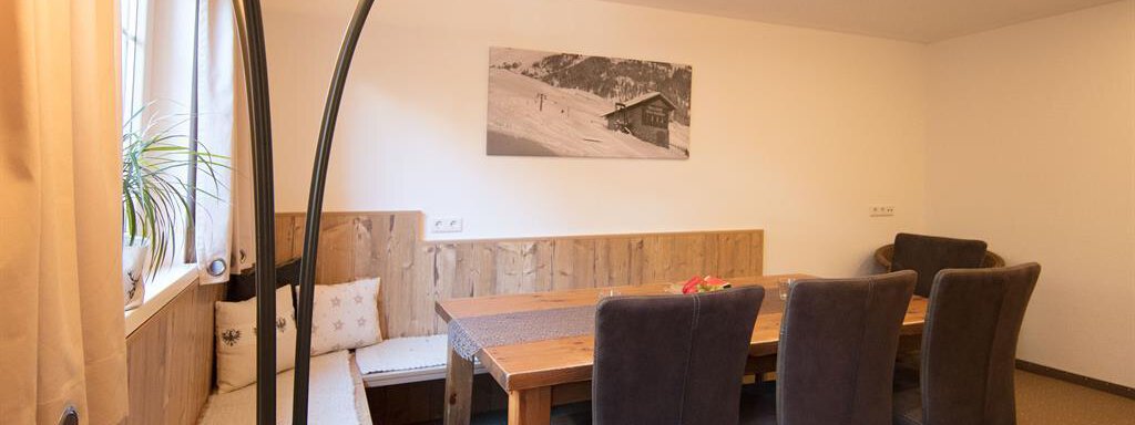 A cozy dining area with a large dining table and modern chairs. Warm light and a wooden bench create an inviting atmosphere. - Haus Gondelblick - Sölden