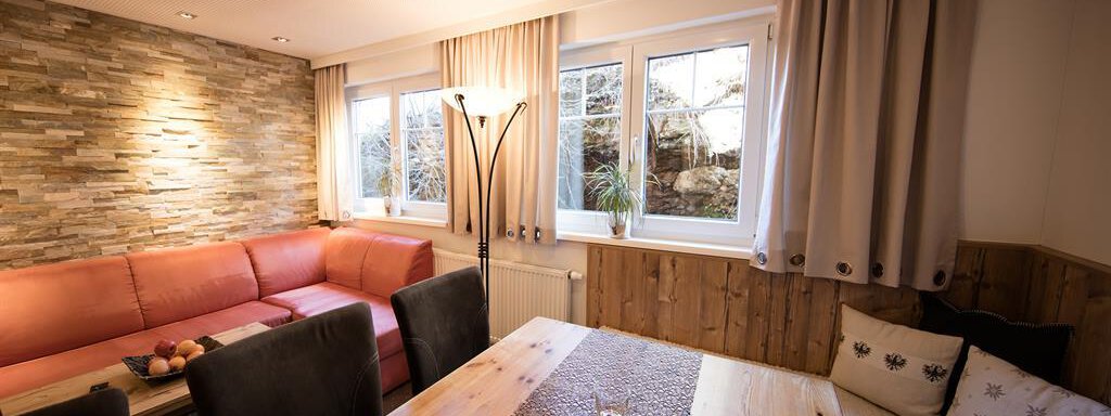 A cozy living room with red sofas and a wooden coffee table.  
Large windows provide plenty of daylight and a view of the outdoors. - Haus Gondelblick - Sölden