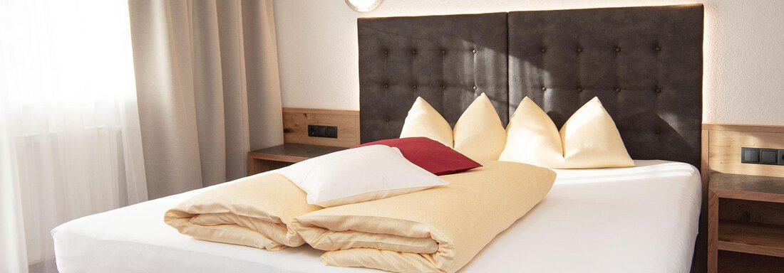 A cozy bedroom with a large bed and bright pillows. On the wall hangs a picture of people in the snow. - Haus Gondelblick - Sölden