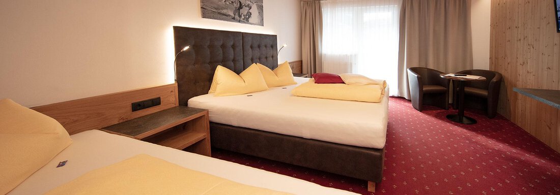 A cozy hotel room with two single beds and yellow bedspreads. The furnishings include a table with chairs and a window with plenty of natural light. - Haus Gondelblick - Sölden