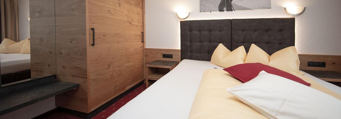 A modern bedroom with a large bed and soft pillows. Wooden details and a decorative picture on the wall create a cozy atmosphere. - Haus Gondelblick - Sölden