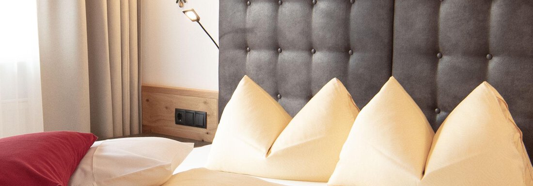 A modern bedroom with a large, upholstered headboard and stylish pillows. The soft lighting creates an inviting atmosphere. - Haus Gondelblick - Sölden